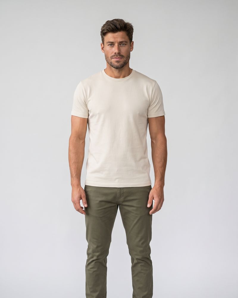 Technicien debout en T-shirt crème, pantalon chino olive et chaussures noires sur fond gris clair